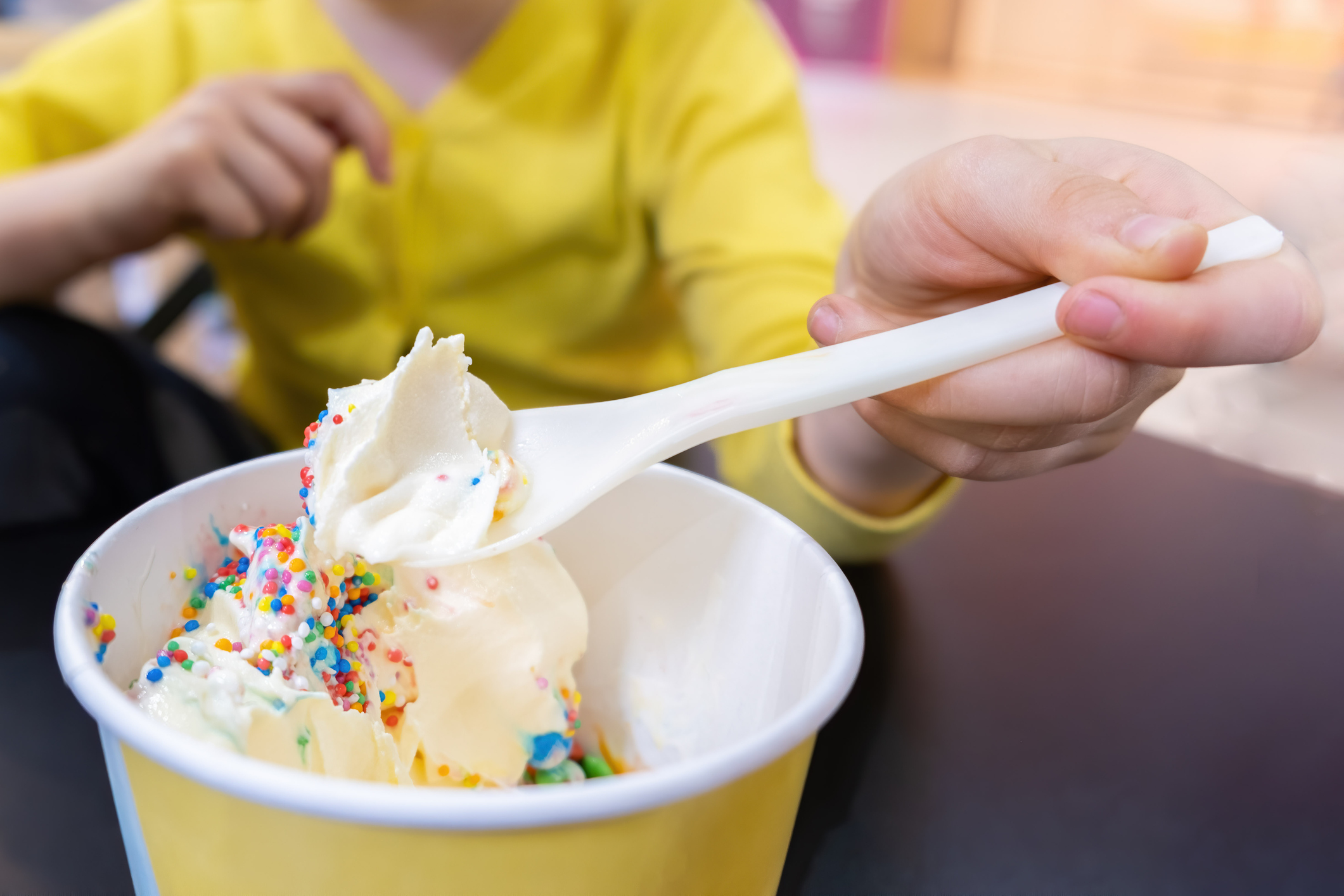 Girl hand holding  white plastic spoon with sweet yogurt and sprinkles - shallow focus