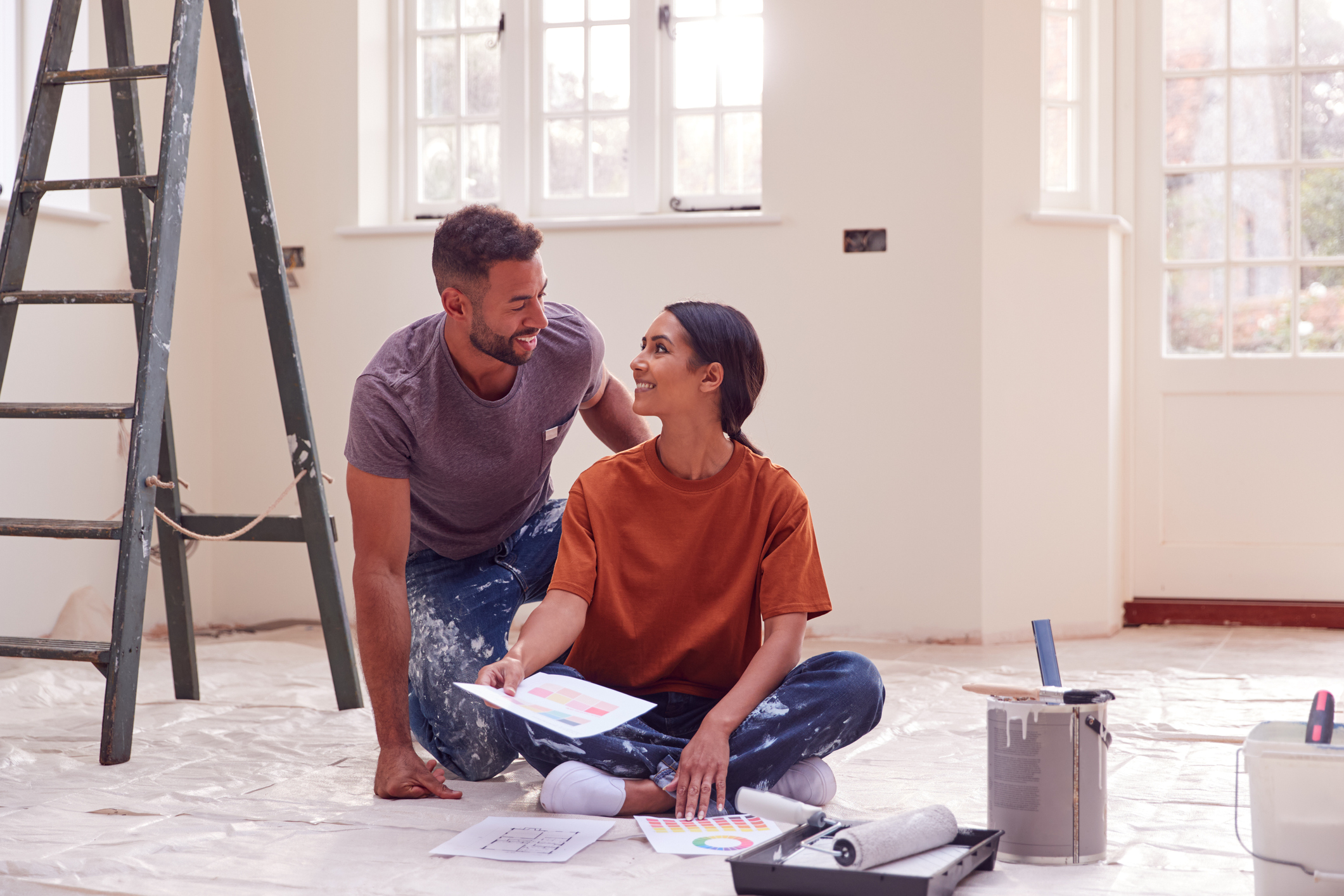Couple Sitting On Floor With Paint Chart Ready To Decorate New Home