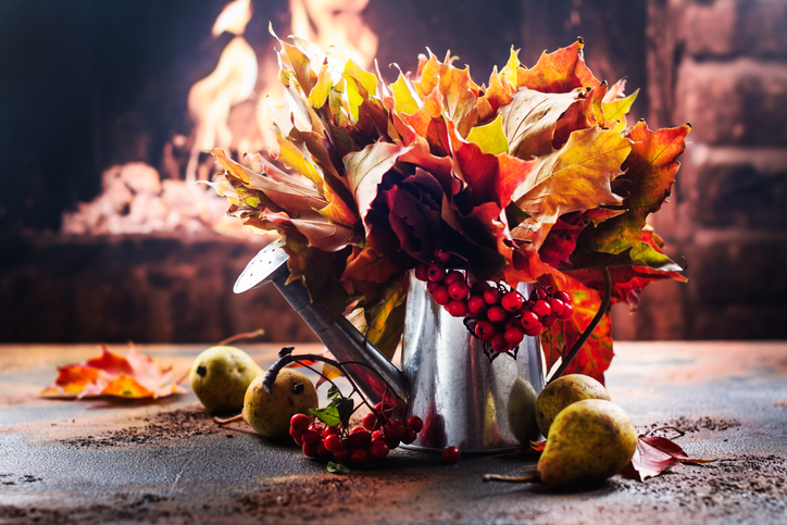 Watering can with autumn leaves and ripe pears near fireplace